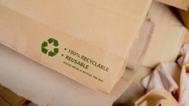 Close-up of brown paper bag with green recycling symbol and '100% RECYCLABLE REUSABLE' printed on it