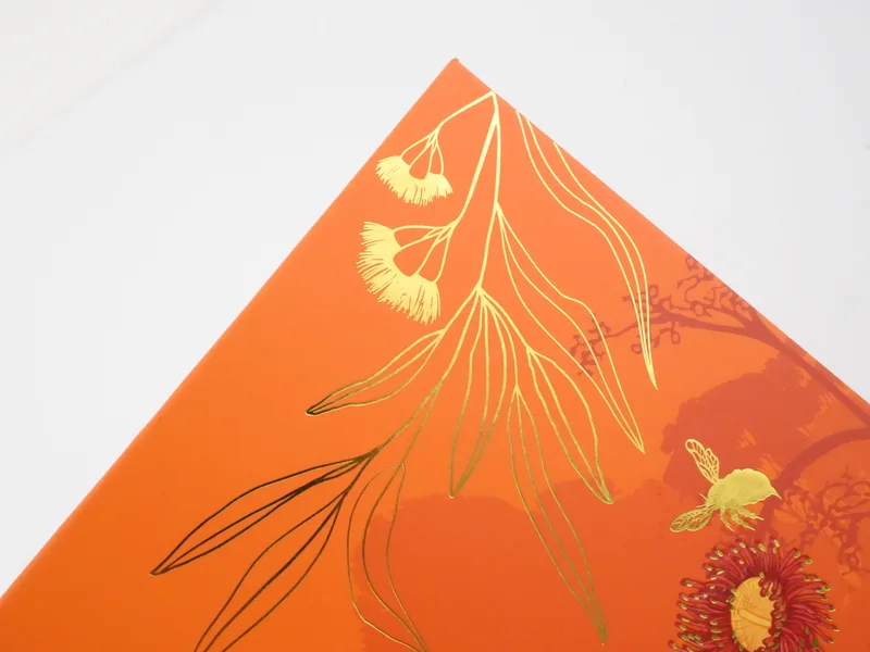 Gold foil stamped eucalyptus leaves and a bee on an orange gift box lid