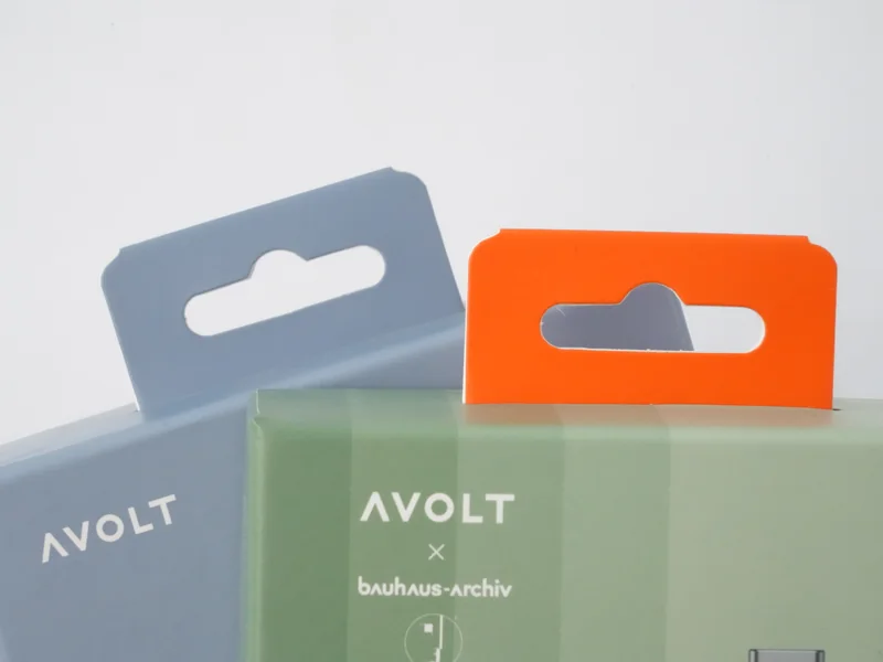 Die-cut paper hanger cards on two retail boxes, one grey and one orange